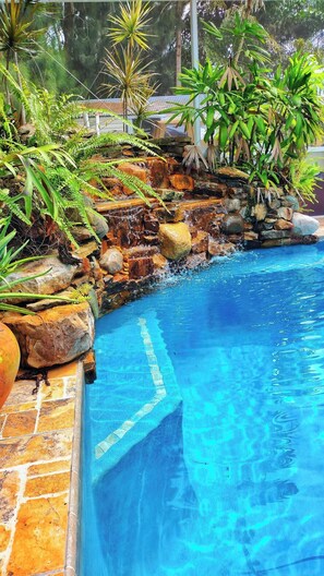 Una piscina con cascada de piedra y plantas tropicales alrededor.