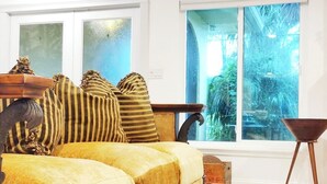 Ein Zimmer mit einer Couch, einem großen Fenster mit Blick auf Grünflächen und einem Vintage-Koffer.