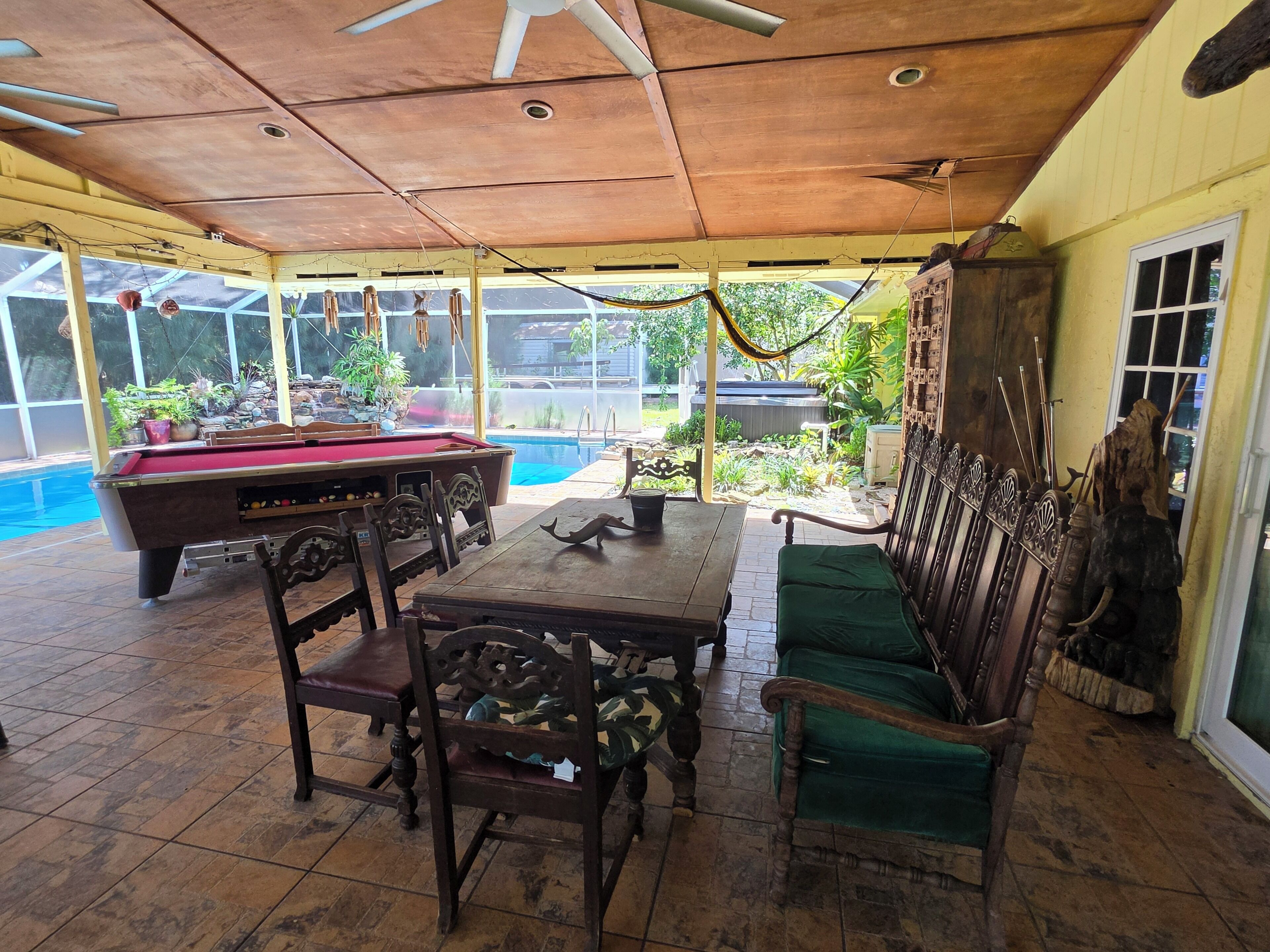 Un espacio al aire libre techado con mesa de billar, sillas y piscina.