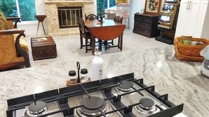 Eine Küche mit Gasherd, weißen Schränken, einem Esstisch mit Stühlen und einem Kamin.