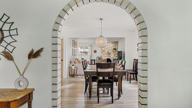 Zona pranzo con arco in mattoni, tavolo in legno, sedie e lampadario.