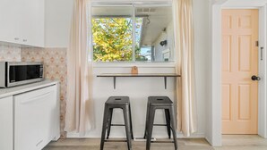 Una piccola cucina con un forno a microonde, due sgabelli, una finestra con tende e una porta.