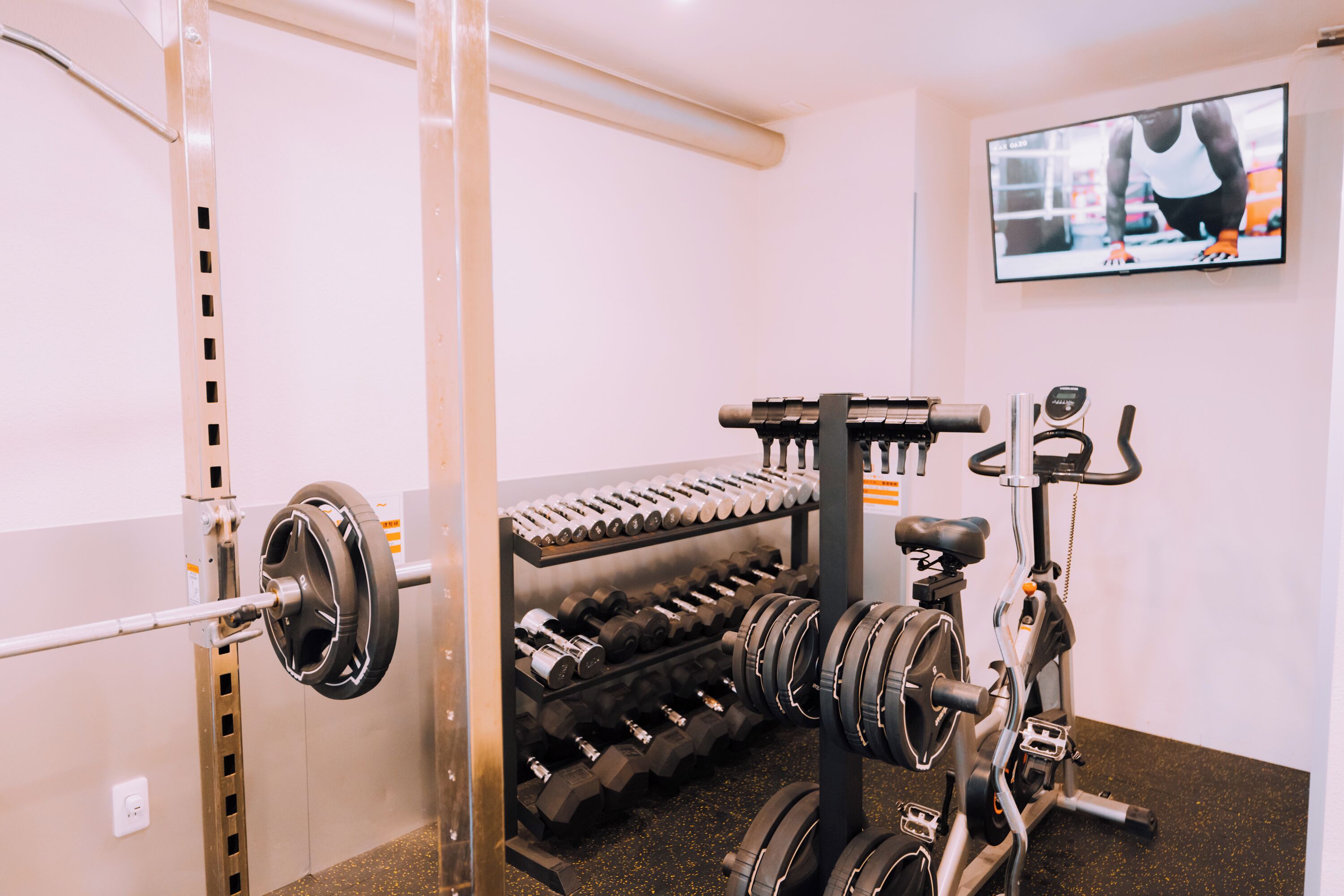 Een sportschool met een rek voor squats, gewichten en een hometrainer.