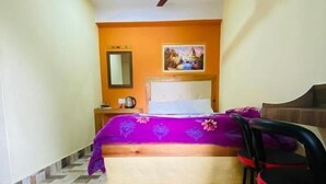 Un dormitorio con cama, ventilador de techo, mesita de noche, silla y un cuadro en la pared.