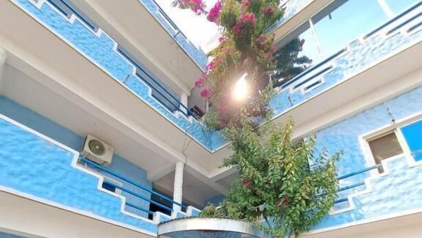 Un edificio de varios pisos con paredes exteriores azules y blancas, un patio central con escaleras y balcones con plantas.