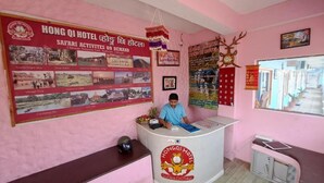 Un mostrador de recepción de hotel con una decoración rosa, un cartel grande que anuncia actividades de safari, y un hombre sentado detrás del mostrador.