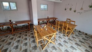 Una habitación con mesas y sillas de madera, un ventilador de techo y plantas colgantes.