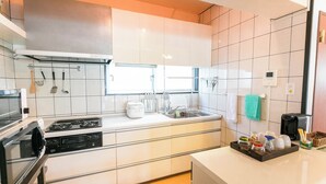 A modern kitchen with white cabinets, a stove, and a sink. There are utensils hanging on the wall and a tray with jars and cups on the counter. - Public Inn Okinawa (Chatan)