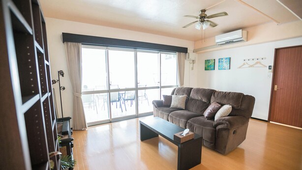A living room with a sofa, a coffee table, and a ceiling fan. - Public Inn Okinawa (Chatan)