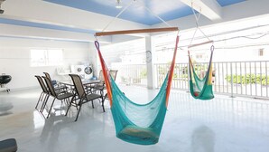A spacious room with a large window, a dining area with chairs and a table, and two hanging hammocks. - Public Inn Okinawa (Chatan)