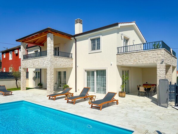 A two-story house with a swimming pool, stone pillars, and a balcony.