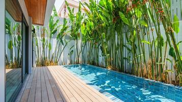 A modern pool area with wooden decking, surrounded by tall tropical plants.