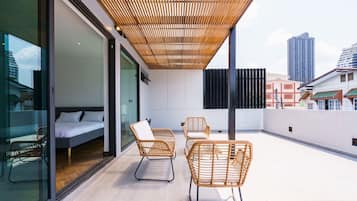 A modern balcony with a bed, two wicker chairs, and a wooden ceiling.