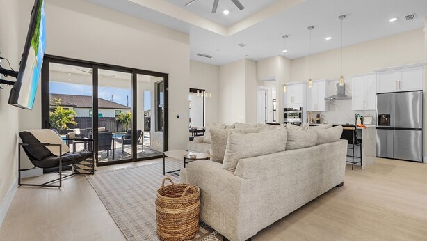 A modern living room with a sofa, a coffee table, and a TV. There is a kitchen area with cabinets and a refrigerator. - Modern 4-bed home with private heated pool, outdoor bar and grill in Cape Coral! (Cape Coral)