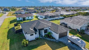 A residential area with modern houses, well-maintained lawns, and a clear sky. - Modern 4-bed home with private heated pool, outdoor bar and grill in Cape Coral! (Cape Coral)
