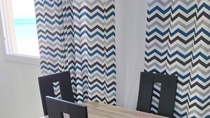 Un comedor con una mesa rectangular y cuatro sillas, una alfombra negra y cortinas con estampado en zigzag.