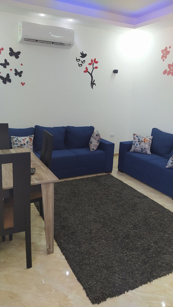 A modern living room with two blue sofas, a wooden coffee table, and a black rug.