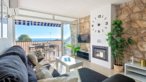 Un salon moderne avec un mur en pierre, une grande horloge, une cheminée et une vue sur la mer.