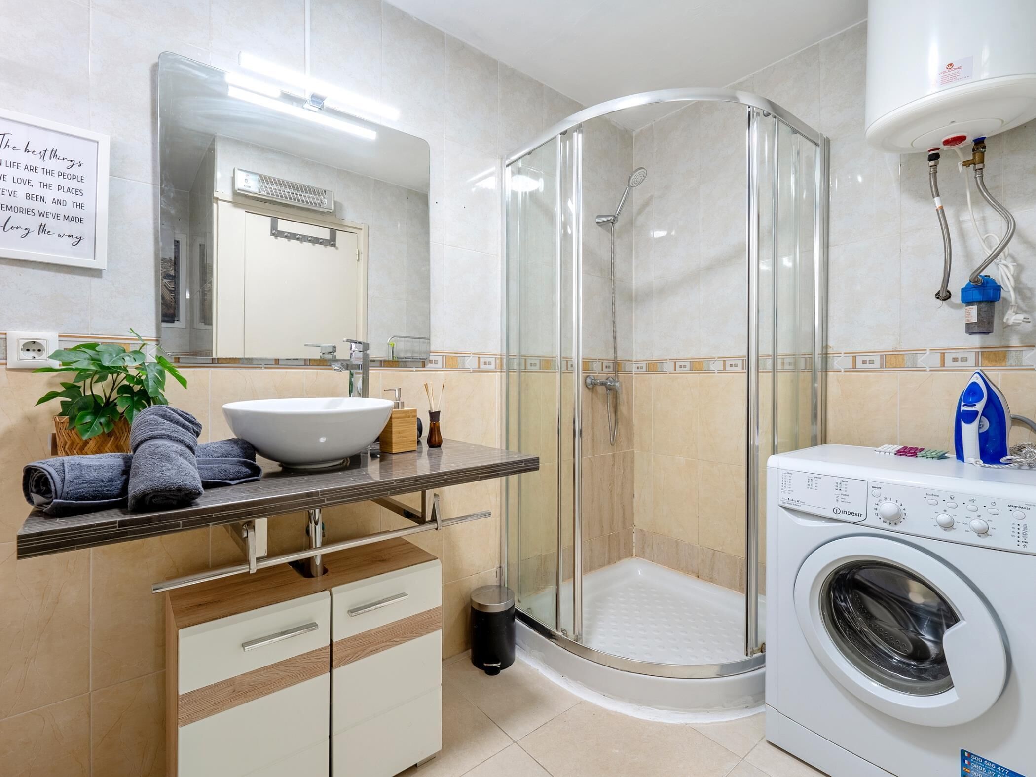 Une salle de bain moderne avec une douche à parois de verre, un lavabo doté d’un grand bac, un lave-linge encastré et un miroir au-dessus du lavabo.