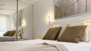 Une chambre d’hôtel moderne avec un grand lit, un miroir, une œuvre d’art accrochée au mur et une table de chevet avec une lampe.