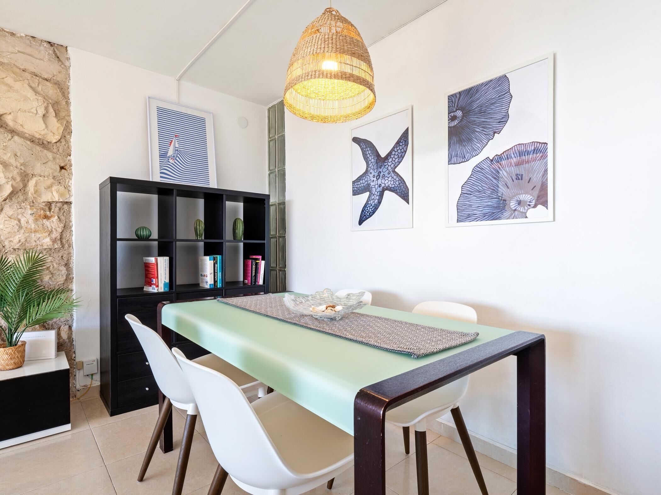 Een eetruimte met een tafel, stoelen, een boekenkast en decoratieve wandkunst.