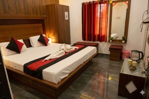A hotel room with a bed, a wardrobe, a mirror, a small table with a kettle, and a red curtain. - Sea Pearl Homestay (Port Blair)