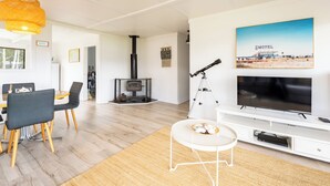 A modern living room with a fireplace, a mounted telescope, a flat-screen TV, and a dining area with chairs and a table. - Askew with a View (Dover)