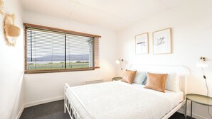 A bedroom with a bed, a window with blinds, a bedside table with a lamp, and two framed pictures on the wall. - Askew with a View (Dover)