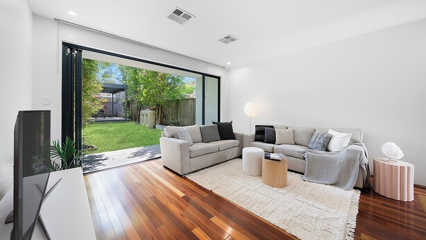 A modern living room with a large sliding glass door leading to a backyard, a grey sofa set, a coffee table, and a TV. - Newtown Family Stay | 6 Beds + Ducted Aircon (Newtown)