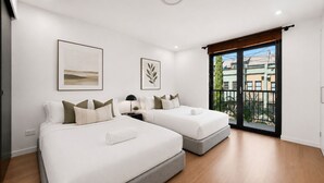 A modern bedroom with two beds, a large window with a view, and a ceiling light. - Newtown Family Stay | 6 Beds + Ducted Aircon (Newtown)