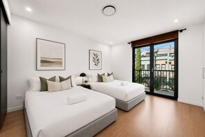 A modern bedroom with two beds, a large window with a view, and a ceiling light.