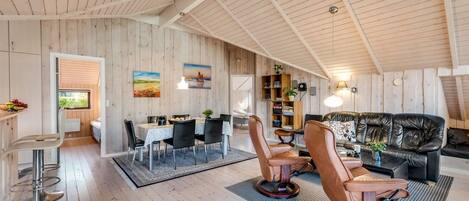 A spacious loft with high ceilings, wooden walls, a dining area, and a cozy seating area with leather chairs and a sofa.