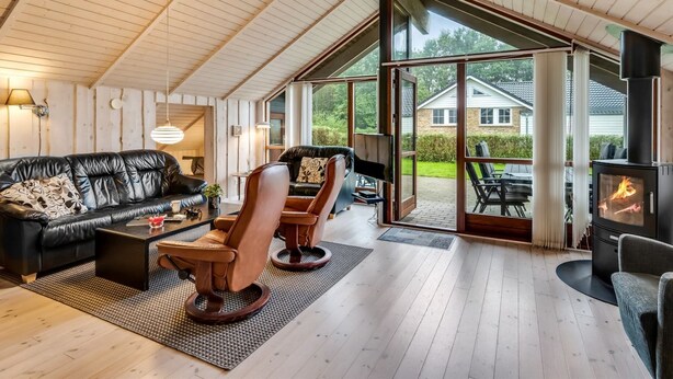 A spacious living area with a wooden ceiling, a black leather sofa, a brown leather armchair, and a glass fireplace. - "Sarah" by Interhome (Ansager)
