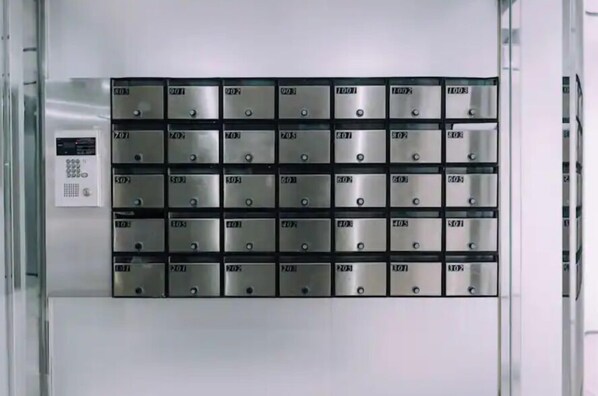 A row of metallic mailboxes with labels, arranged in a grid pattern on a wall.