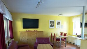Un salon comprenant un canapé, une petite table, un téléviseur et un coin repas avec des chaises et une table.