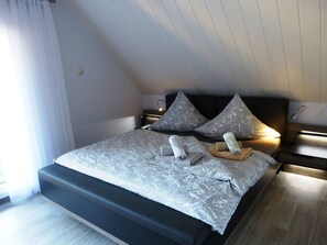 A modern bedroom with a large bed, two pillows, a bedside table, and a nightstand.