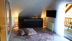 Une pièce chaleureuse avec un plafond en pente, un téléviseur à écran plat fixé au mur, un meuble en bois et un tapis à motifs.