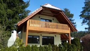 Un chalet à deux étages doté d’un balcon en bois, de grandes fenêtres et d’un toit à pente.