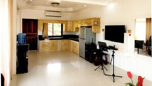 Una cucina moderna con mobili in legno, un piano di lavoro nero e un piano cottura integrato. È presente un'ampia finestra con tende, un dispenser d'acqua e un televisore a schermo piatto montato a parete.