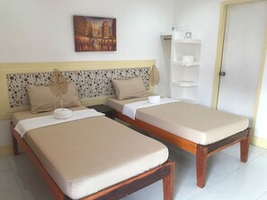 A hotel room with two beds, a decorative wall panel, a painting, and a white shelf with toiletries. - Bountiful Inn (Puerto Princesa)