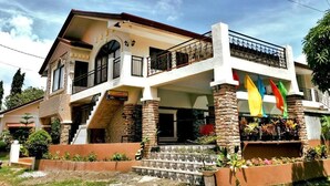 Una casa a due piani con un balcone, una scalinata e un giardino con piante.