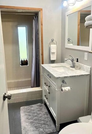 Een badkamer met een douche, een wastafel, een spiegel en een toilet.