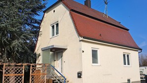 A two-story house with a red roof, a visible staircase, and a small porch area. - Family House (Bibertal)