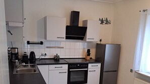 A modern kitchen with white cabinets, a built-in oven, a refrigerator, and a coffee maker. - Family House (Bibertal)