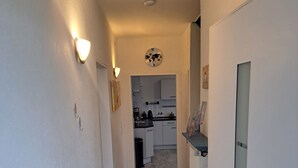 A hallway with wooden flooring leading to a kitchen area with white cabinets and a clock on the wall. - Family House (Bibertal)