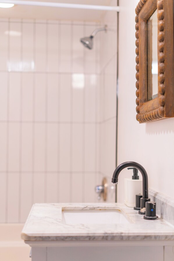 Une salle de bain avec un lavabo en marbre, un miroir encadré en bois et un espace douche.