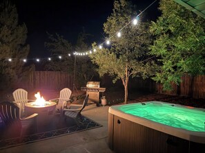 Une terrasse extérieure avec un foyer, deux fauteuils Adirondack, un jacuzzi et un barbecue.