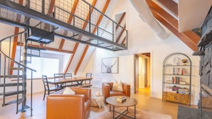 Un ampio loft con soffitto alto, travi a vista in legno, una scala a chiocciola, mobili in pelle, un camino e una libreria.