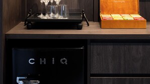Un mueble de madera con una bandeja que contiene copas de vino y una caja etiquetada como “TWININGS of London” con bombones.