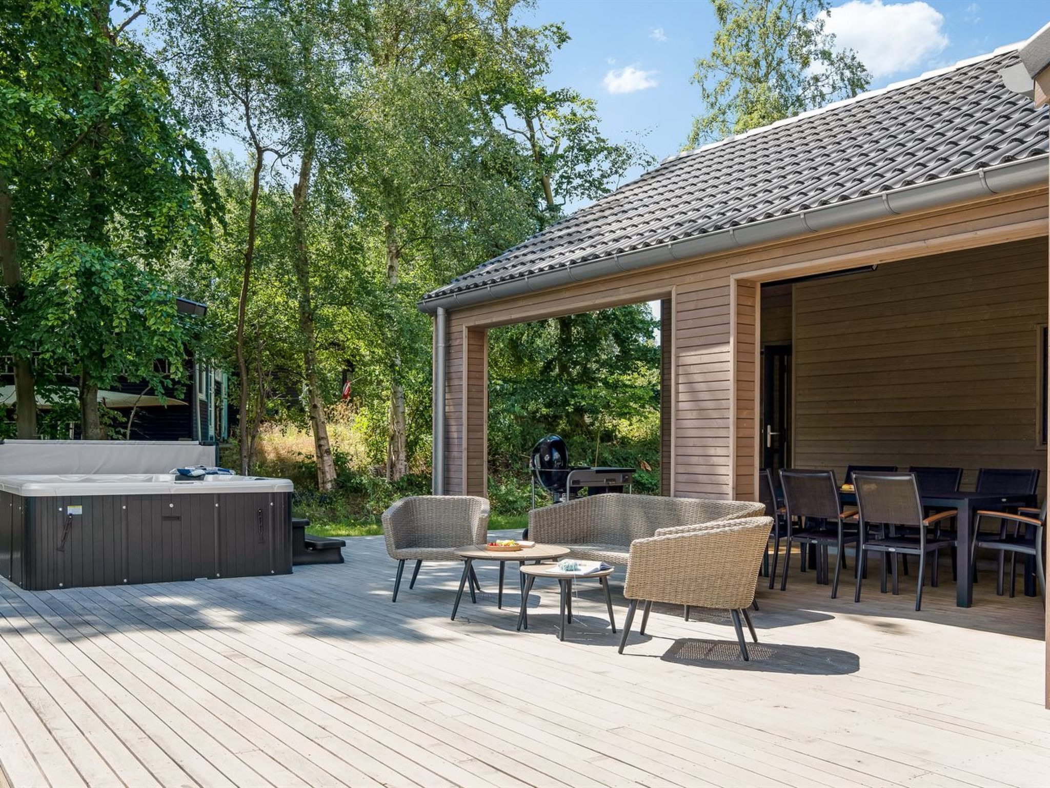 A covered outdoor patio with a hot tub, wicker furniture, and a grill area.